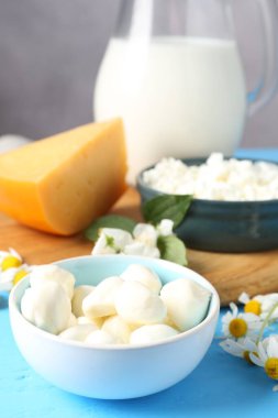 Açık mavi ahşap masa üzerinde farklı taze süt ürünleri ve çiçekler.