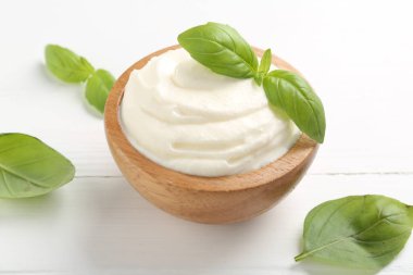 Lezzetli yoğurt kasede fesleğen beyaz ahşap masada, yakın plan.