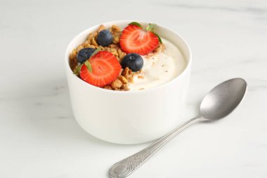 Tahıllı yoğurt, beyaz mermer masada böğürtlen ve kaşık, yakın plan.