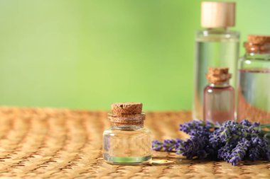 Hasır masanın üzerinde lavanta yağı ve çiçek şişeleri, yakın plan. Metin için boşluk