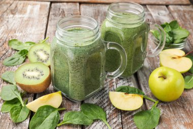 Duvarcı kavanozunda nefis bir smoothie, ıspanak yaprakları, elmalar ve kivi renkli ahşap masa, yakın plan.