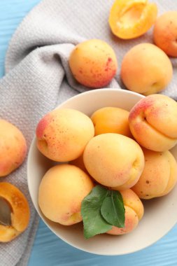 Açık mavi ahşap masa üzerinde yeşil yapraklı taze kayısılar.