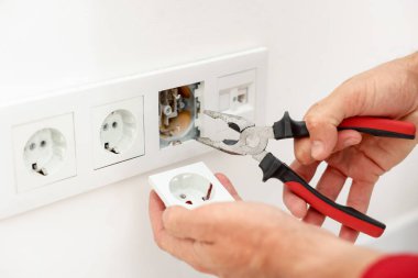 Kapalı mekanda penseyle prizleri tamir eden adam, yakın plan.