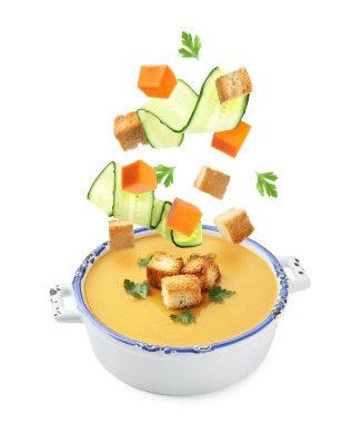 Cruton, salatalık dilimleri ve balkabağı küpleri beyaz arka planda çorba kasesine düşüyorlar.