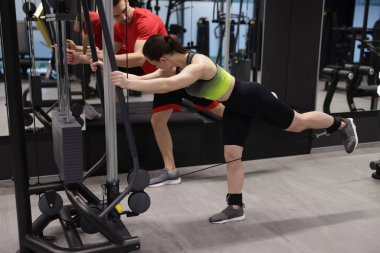 Genç bir kadın spor salonunda profesyonel antrenörle kablolu TV ile egzersiz yapıyor.