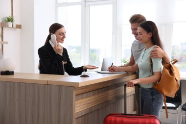 Otel resepsiyonunda müşterilerle çalışan gülümseyen bir resepsiyonist.