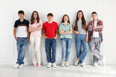 Beyaz duvarın yanında poz veren bir grup mutlu genç.