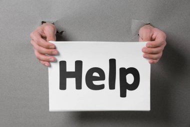 Yardım istemek ya da teklif etmek. Gri kağıtlardaki deliklerden kağıt tutan adam, yakın plan.