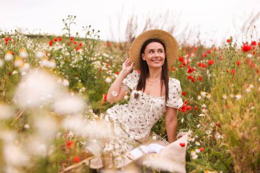 Gülen kadın şapkalı yaban çiçeği çayırında doğanın tadını çıkarıyor.