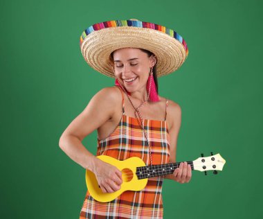Yeşil arka planda ukulele çalan şapkalı gülümseyen kadın.