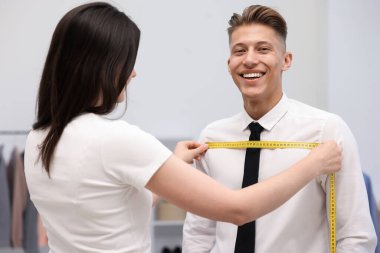 Atölyede bantla adamın göğsünü ölçen terzi.