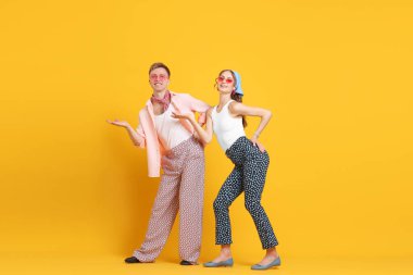 Turuncu arka planda dans eden retro kıyafetli mutlu çift.