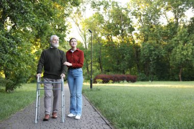 Gülümseyen bakıcı dışarıda yürüyen çerçeveyi kullanan yaşlı bir adamı destekliyor. Metin için boşluk