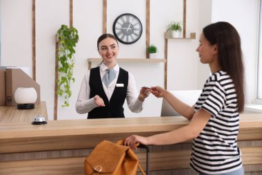 Üniformalı gülümseyen resepsiyonist otel odasındaki konuklara anahtar kartı veriyor.