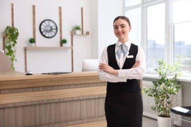 Otelde kollarını kavuşturmuş gülümseyen resepsiyonistin portresi.