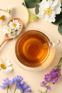 Cam fincanda Aromatik bitki çayı ve bej arka planda farklı çiçekler, düz uzanma