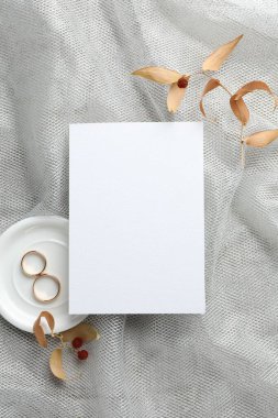 Düğün davetiyesi, altın yüzükler ve gri tül kumaş üzerinde kuru yapraklar.