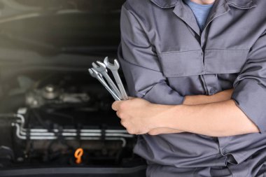 Otomobil parçaları. Kaputu açık, kapalı kaputun yanında anahtarı olan profesyonel bir tamirci, yakın plan. Metin için boşluk