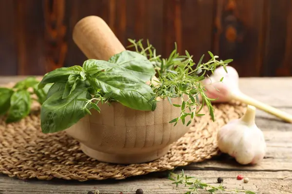 Kabuklu havan, farklı aromatik otlar ve baharatlar ahşap masada, yakın plan.