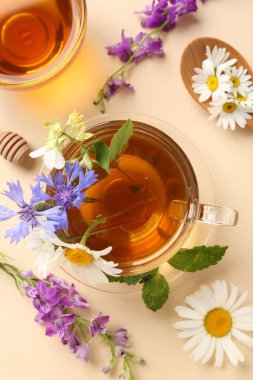 Cam fincanlarda aromatik bitki çayı, farklı çiçekler ve bej arka planda nane şekeri, düz uzanmış