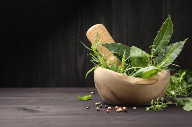 Farklı taze bitkilerle havan topu, biber ve ahşap masa üzerinde koyu arkaplan, yakın plan. Metin için boşluk