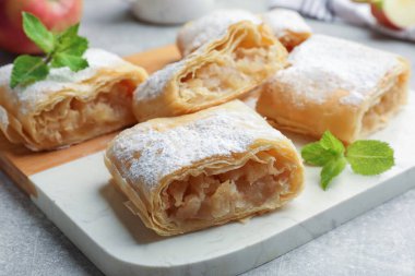 Lezzetli elmalı turta parçaları pudra şekeri ve açık gri masada nane şekeri, yakın plan.