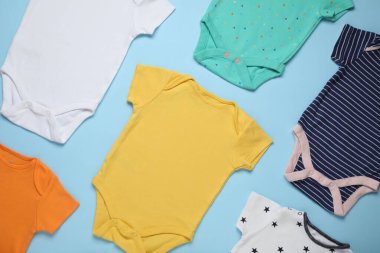 Açık mavi arkaplanda farklı bebek tulumları, düz yatış.