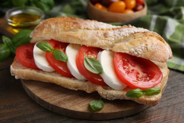 Mozarella peynirli, domatesli ve ahşap masadaki fesleğenli lezzetli sandviç.