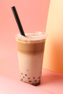 Pembe arka planda plastik fincanda lezzetli sütlü çay, yakın plan.