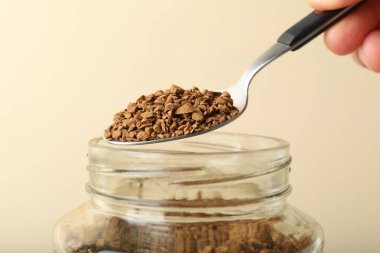 Bej arka planda kaşıkla hazır kahve alan kadın, yakın plan.