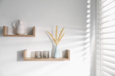 Masa takımları ve beyaz duvarda vazolar olan ahşap raflar.