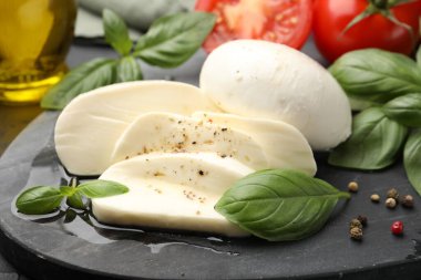 Lezzetli mozzarella peyniri, domates, fesleğen ve baharatlar masada, yakın plan.