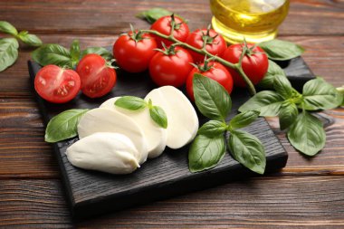 Lezzetli mozzarella peyniri, domates ve fesleğen ahşap masada, yakın plan.