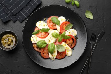 Peynirli Caprese salatası, domates, fesleğen ve baharatlar siyah masada, düz yerde.