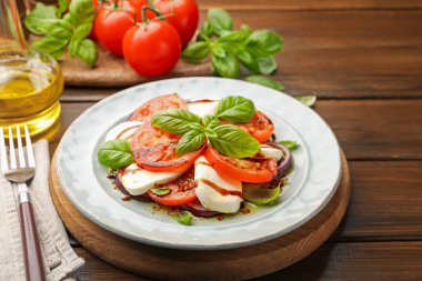 Mozarella, domates, fesleğen ve baharatlarla ahşap masaya yakın plan Caprese salatası.