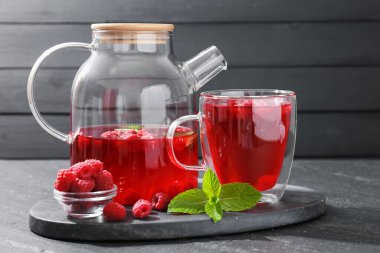 Cam fincanda Aromatik ahududu çayı, çaydanlık, böğürtlen ve nane, siyah masada yakın plan.