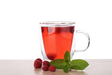 Aromatik ahududu çayı cam fincanda, böğürtlen ve yeşil yapraklar ahşap masada beyaz arka planda