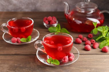 Cam bardaklarda ahududu çayı, çaydanlık, böğürtlen ve nane şekeri ahşap masada, yakın plan.