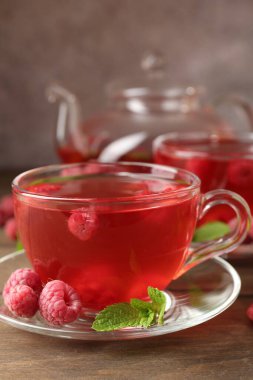 Cam bardaklarda ahududu çayı, çaydanlık, böğürtlen ve nane şekeri ahşap masada, yakın plan.