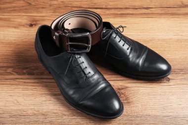 Ahşap yüzeyde siyah deri ayakkabılar ve kemer, yakın plan.