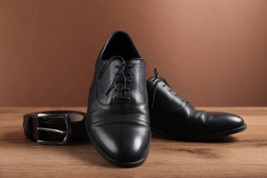 Bir çift siyah deri ayakkabı ve kemer ahşap zeminde kahverengi arka planda, yakın plan