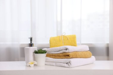 İçerideki beyaz masada renkli havlu, sıvı sabun ve çiçek dekoru yığını.,