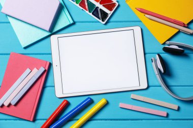 Tablet, farklı kırtasiye malzemeleri ve kulaklıklar açık mavi ahşap masa, düz uzanma