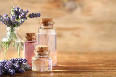 Ahşap masa üzerinde lavanta yağı ve çiçek şişeleri, yakın plan. Metin için boşluk