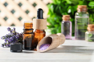 Beyaz ahşap masa üzerinde gerekli yağ, çiçek ve deniz tuzu şişeleri, yakın plan.