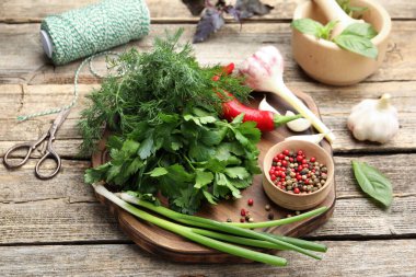 Farklı taze otlar, baharatlar, makas, iplik, havan ve tokmak, ahşap masa, yakın plan.