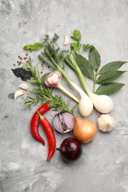 Farklı taze otlar, sarımsak, soğan ve diğer baharatlar gri masada, düz yerde.
