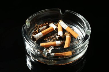 Sigara izmaritleri siyah arka planda kül tablasında, yakın plan.