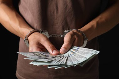 Yozlaşma. Elleri kelepçeli bir adam siyah arka planda dolarları tutuyor.