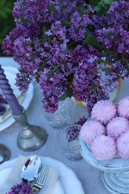 Güzel leylak çiçekleri, zephyrler, tabaklar, çatal bıçak takımı ve mumlar bahçede, üst tarafta.